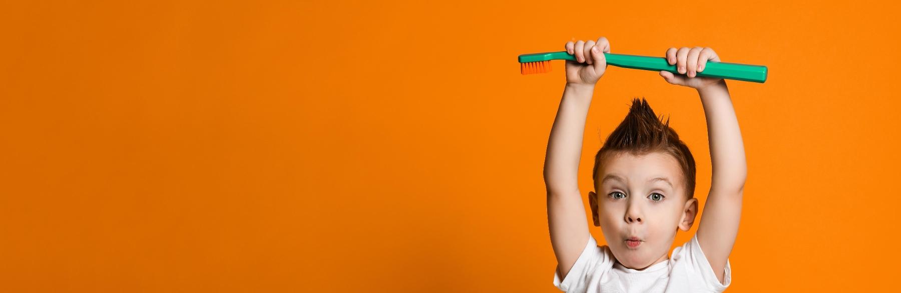Young boy holding up a tooth brush at pediatric dentist in Webster Groves MO