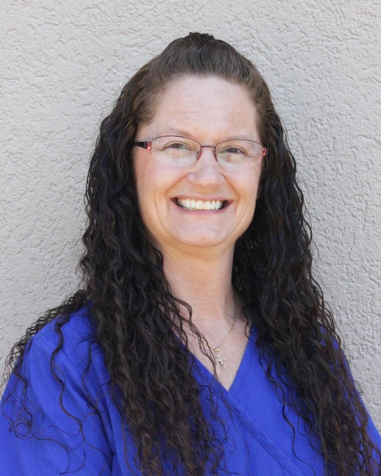 professional headshot of a smiling woman with glasses in blue scrubs