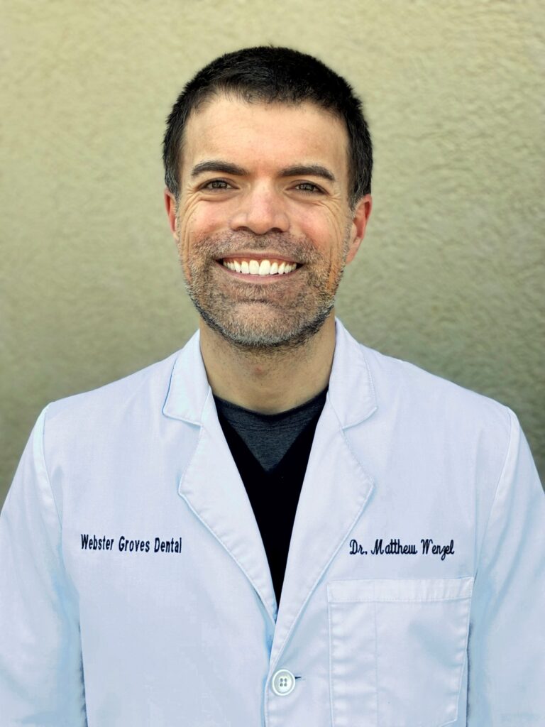 professional headshot of a smiling male dentist in a white coat